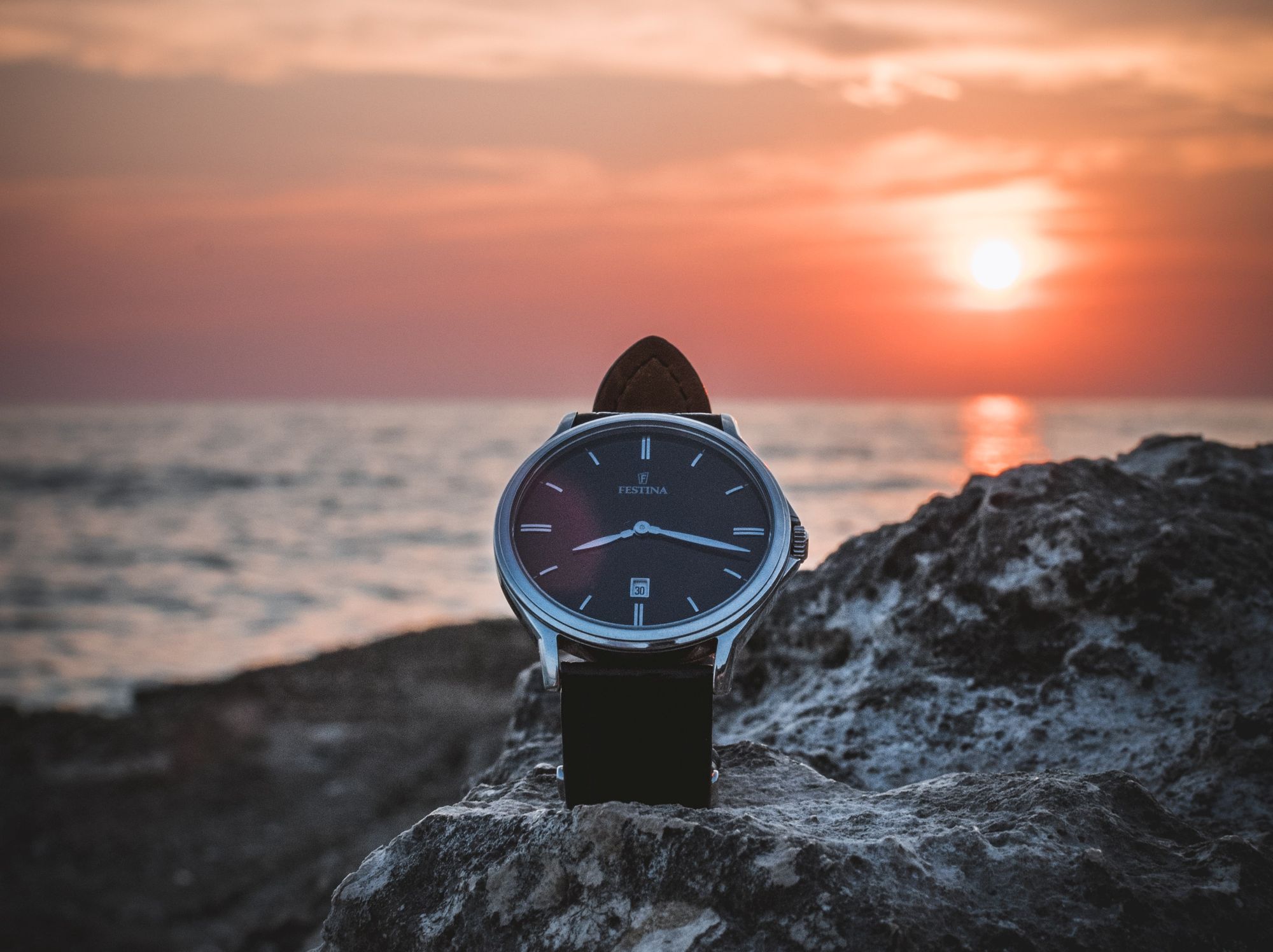 Picture of a watch sitting on a rock on the beach during the sunset